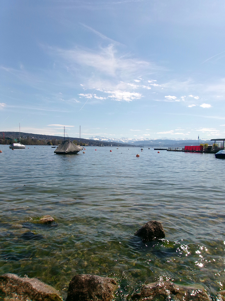 Clear alpine lake with boats and snow-capped mountains in the distance