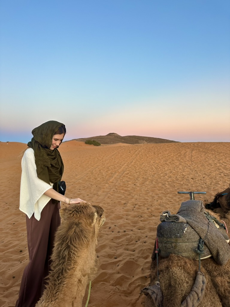 Kendyll petting a camel in the desert at sunset