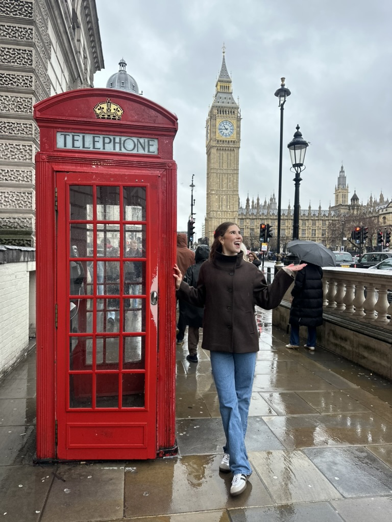 Kendyll smiling by a red London phone booth with Big Ben in the background